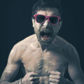 Portrait photographique d’Olivier Giner réalisé par le photographe Henri Aubron, ambiance sombre et punk avec lunettes roses
